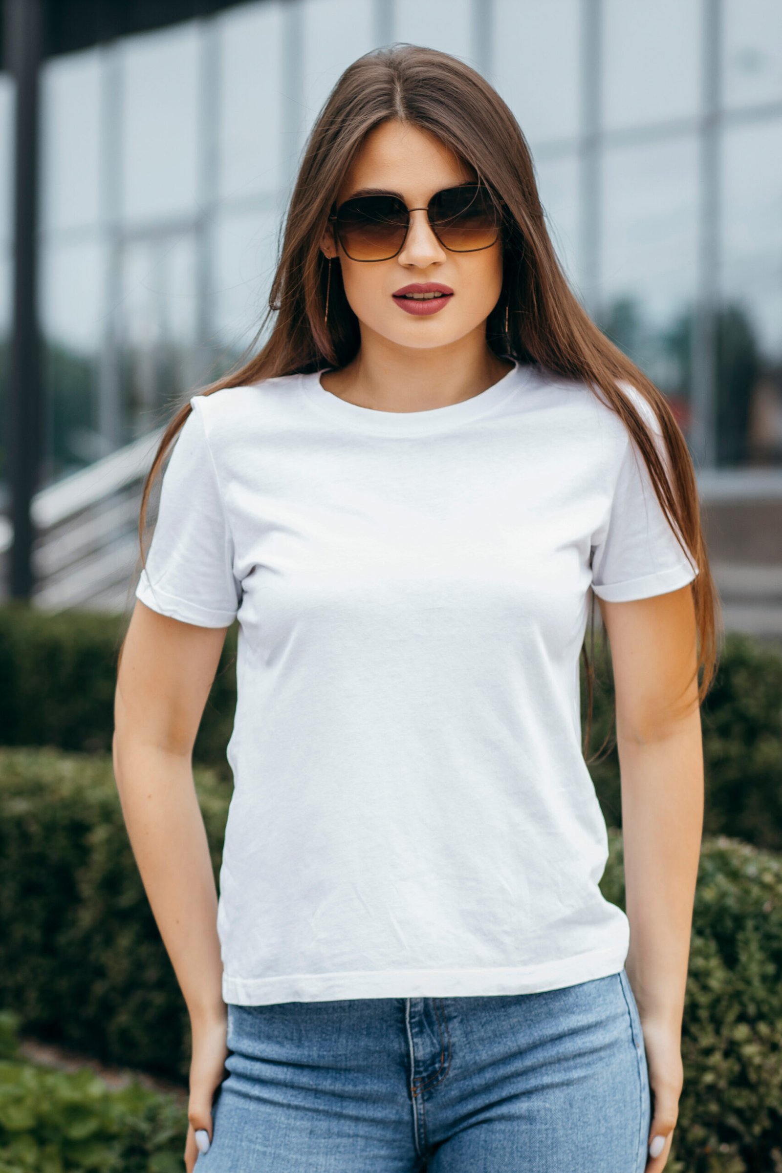 stylish brunette girl wearing bwhite t shirt and glasses posing against street , urban clothing style. street photography